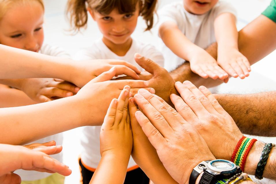 Kinder und Erwachsene legen ihre Hände in einem Kreis zusammen, symbolisieren Zusammenarbeit und Gemeinschaft.